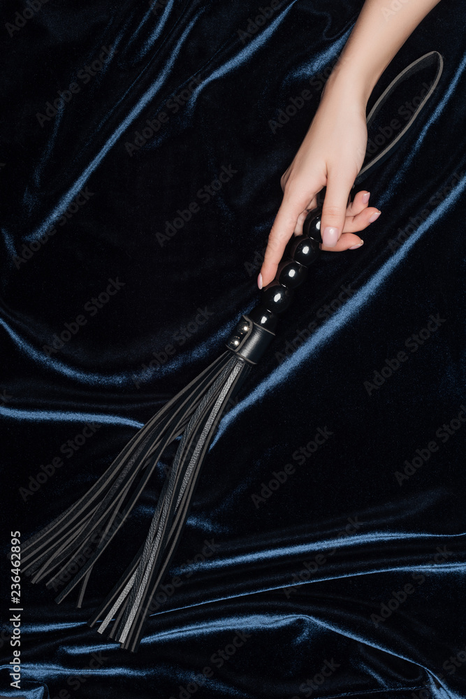 cropped view of female hand holding flogging whip with shiny velvet cloth at background