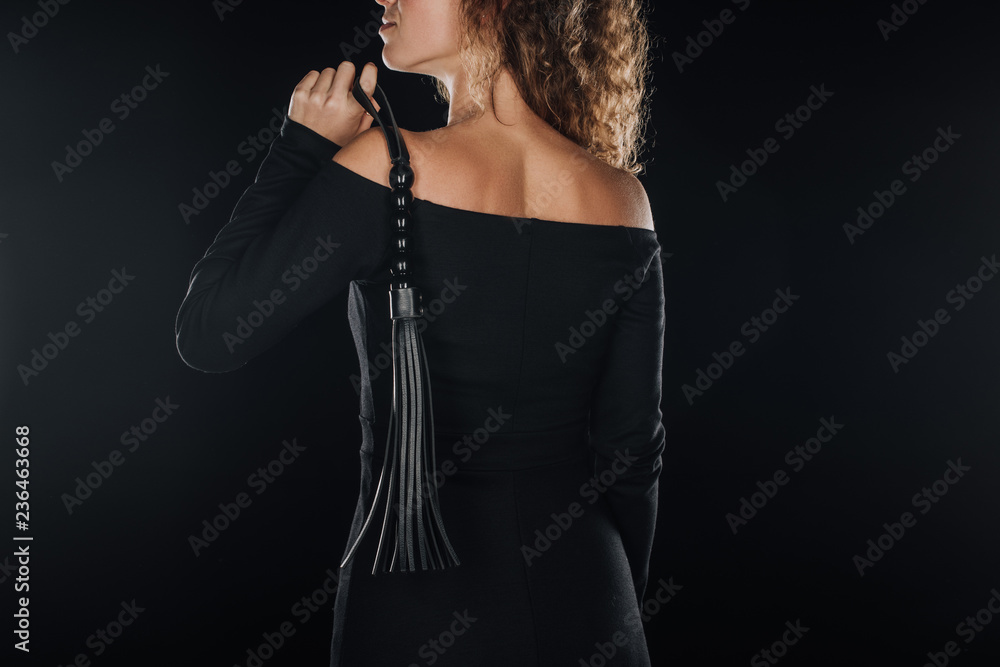 back view of adult woman holding flogging whip isolated on black
