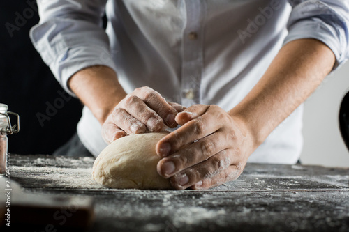 Fototapeta Naklejka Na Ścianę i Meble -  Cook kneads dough with flour on kitchen table