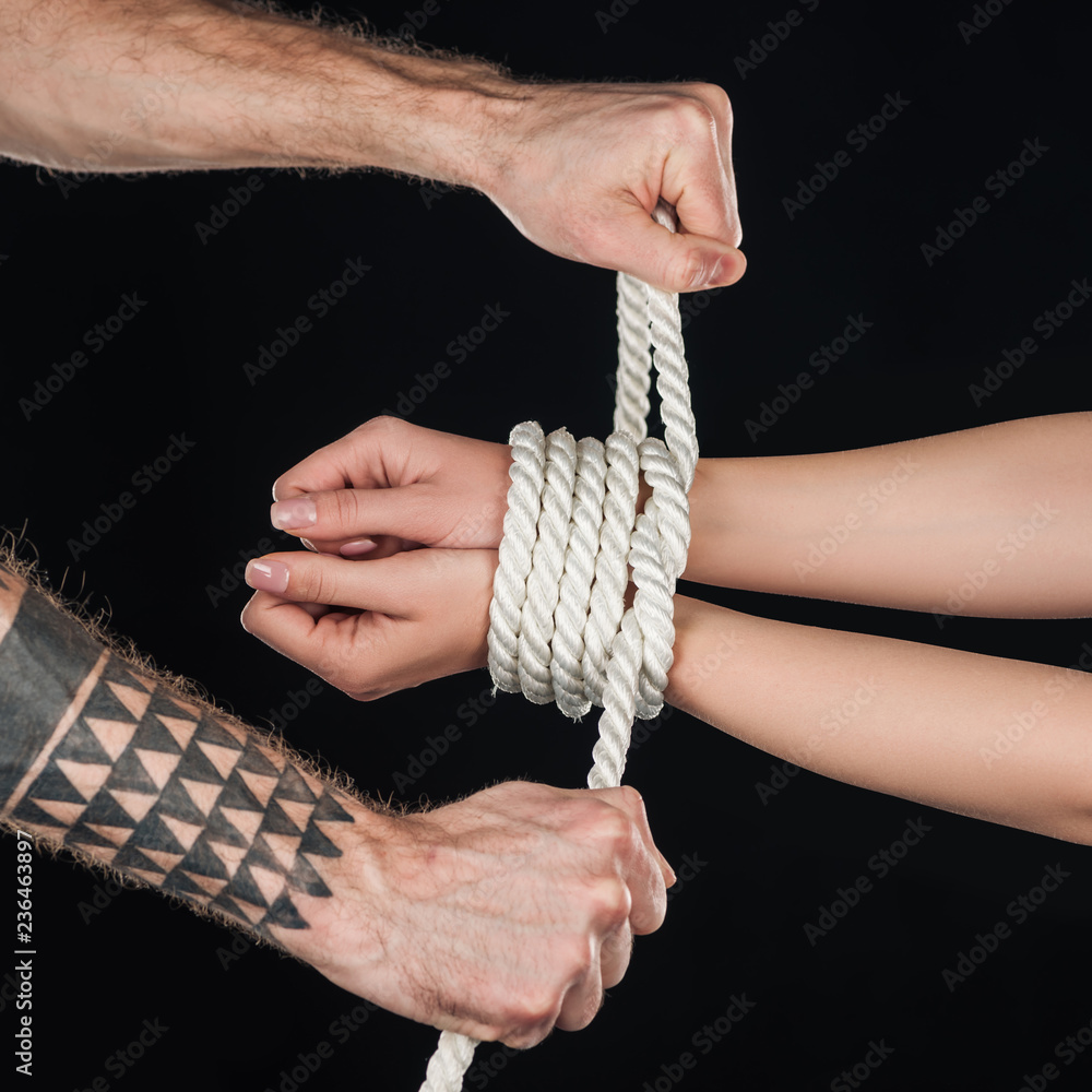 close up of tattooed man tying rope on female hands isolated on