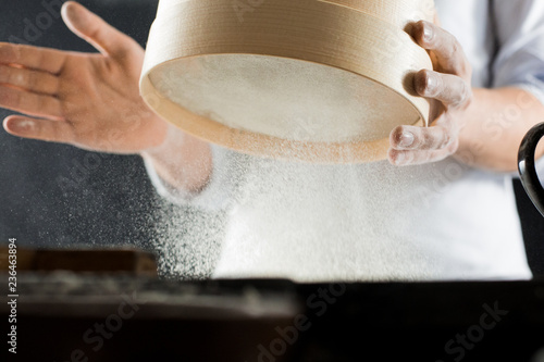 Male hands of a cook sifting flour through a sieve in the kitchen