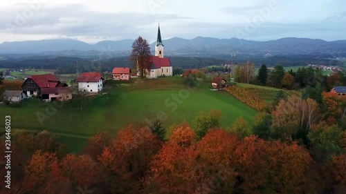 Aerial: Flying on early autumn morning sunrise over Slovenian countryside. Going over beautiful forest towards small church on top of the hill.