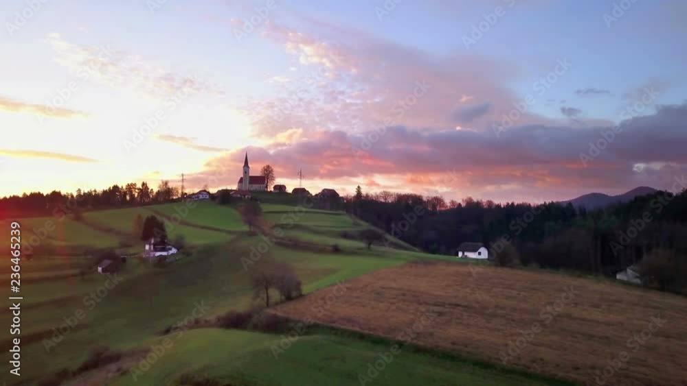 Aerial: Flying on early autumn morning sunrise over Slovenian countryside. Going over beautiful green meadows and fields towards small church on top of the hill. Aerial: Flying on early autumn morning sunrise over Slovenian countryside. Going over beautiful green meadows and fields towards small church on top of the hill.
