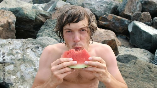 Portrait of a handsome young man eating with a slice of watermelon in his hands photo