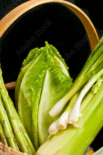 Front view, close distance of a weaved wood basket of freshly cut, local, organic vegetables of romaine lettuce, green onions and celery photo