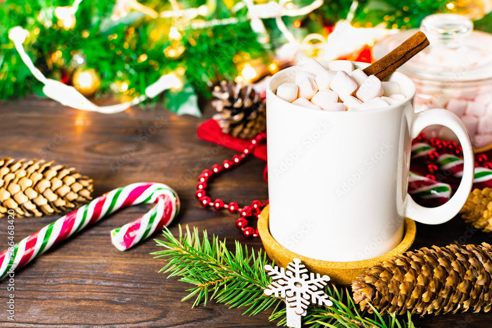White mug of cocoa with marshmallows, lollipops, fir cones, Christmas tree branch, garland and snowflake on wooden table White mug of cocoa with marshmallows, lollipops, fir cones, Christmas tree branch, garland and snowflake on wooden table