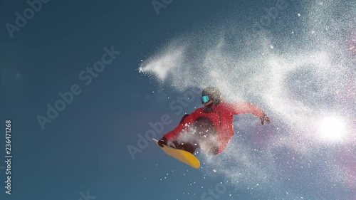 SLOW MOTION CLOSE UP: Snowboarder jumping big air kicker, spraying snowflakes and flying over sun on perfect winter day. Snowboard jump in snow park. Sunbeams shining past jumping boarder in mountains