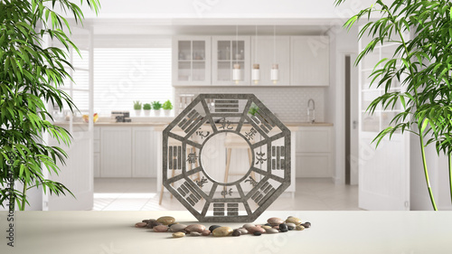 Fototapeta Biała półka stołowa z bagua, kamienistymi kamieniami i bambusowymi roślinami, biała skandynawska kuchnia z wyspą i dużymi drzwiami, projekt wnętrz zen concept, szablon pomysłów feng shui