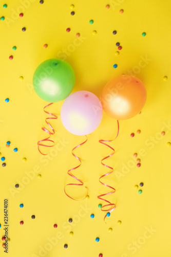Three colorful balloons, candies and confetti on yellow background. Birthday, holiday or party background.