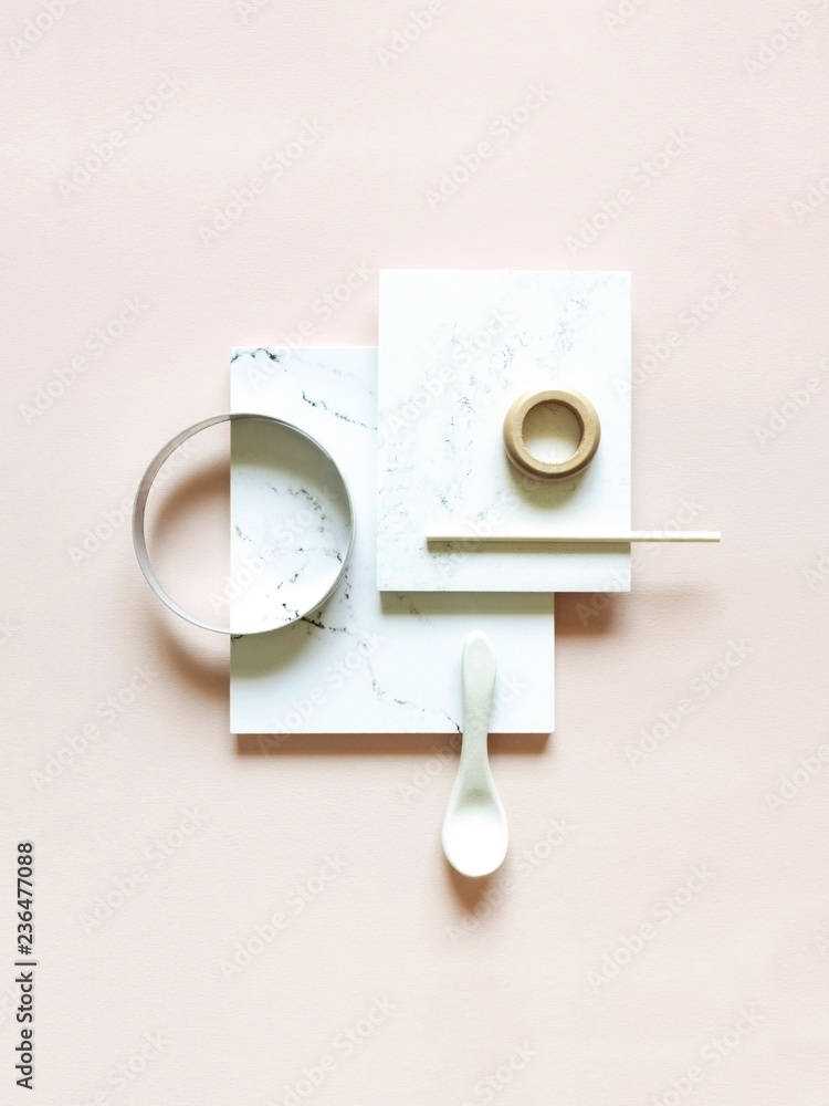 A still life flat-lay arrangement of various white and marble objects on a pale pink background.
