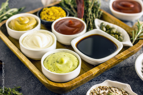 A set of popular sauces and spices close up on a stone background: mayonnaise, ketchup, owl sauce, cheese sauce, mustard, pepper, turmeric, rosemary, turmeric, ginger