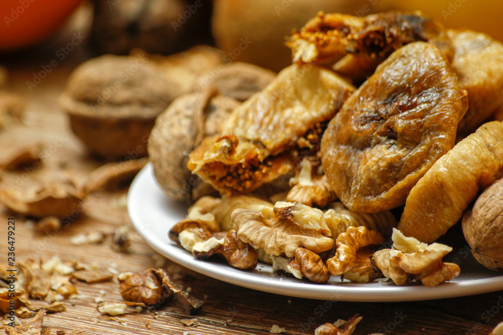 Dried fig and whole and cracked walnuts on white ceramic plate. Wooden table and various citrus in the background.