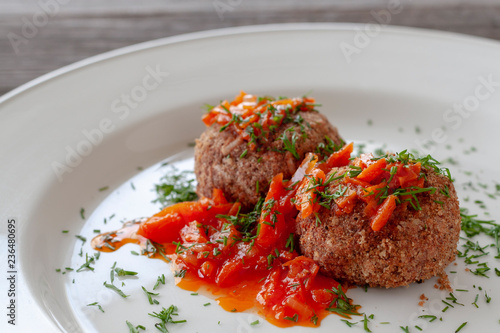 Bean meatballs with sweet pepper sauce on a white plate, decorated with herbs.