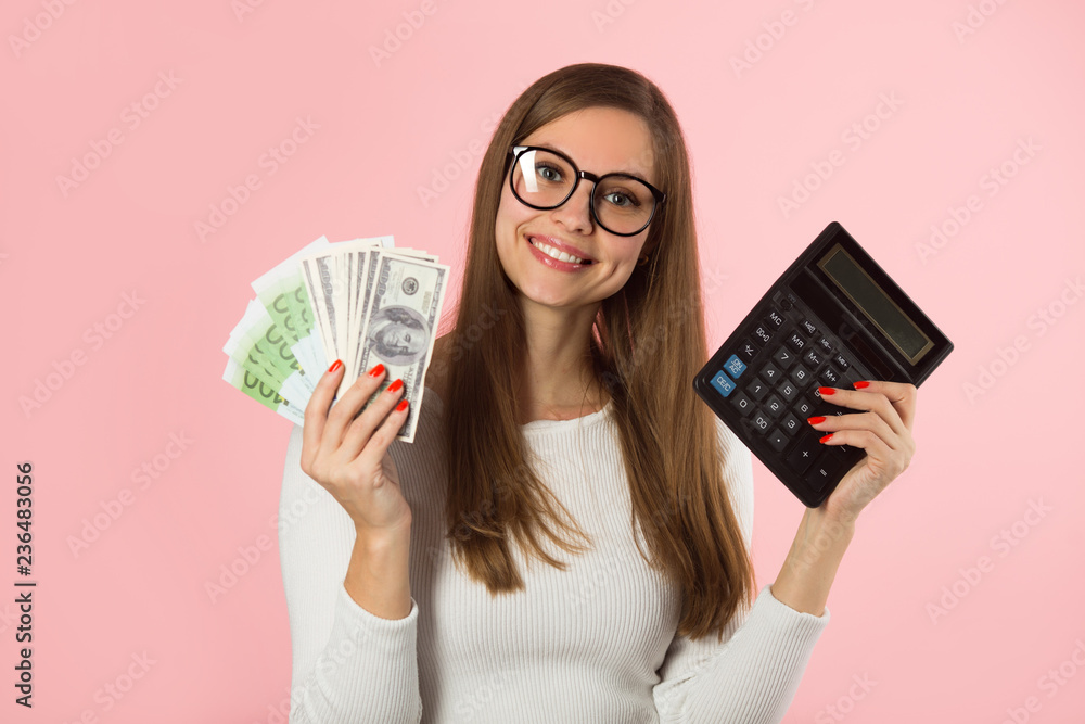 beautiful young girl in glasses with money and a calculator in her hands on a pink background beautiful young girl in glasses with money and a calculator in her hands on a pink background
