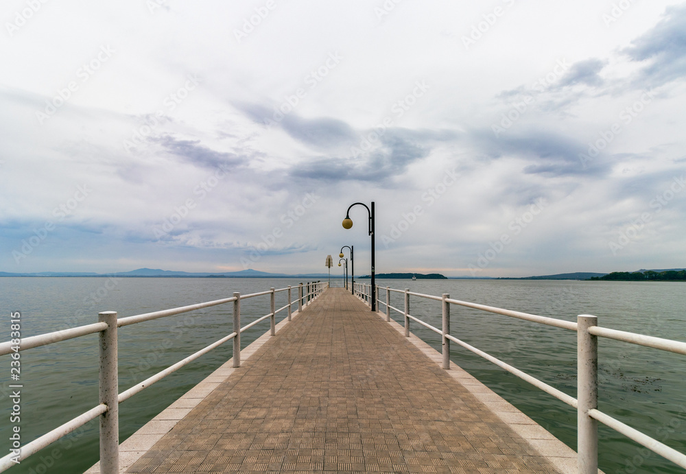 Beautiful view of Lake Trasimeno from the pier.  The sky is clouded over and calm water, no people. Nostalgic mood. Umbria, Italy