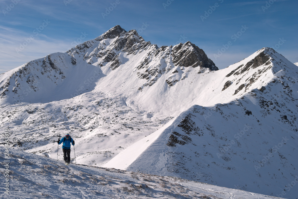 Ski mountaineer with snowy rocky mountain peak in the background finding his own individual way to the summit.