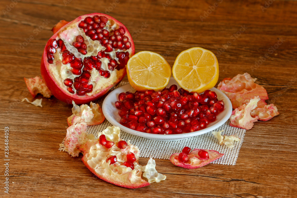 Ripe pomegranate and lemon on a ceramic plate. Close-up, wooden table and rustic background. Ripe pomegranate and lemon on a ceramic plate. Close-up, wooden table and rustic background.