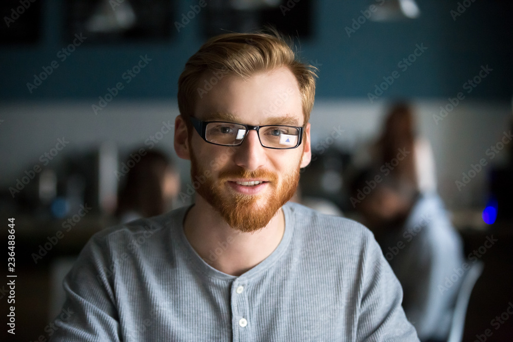 Portrait of smiling red haired millennial man looking at camera sitting in cafe or coffeeshop, happy young male in glasses posing for picture working at laptop or studying out in coffeehouse Portrait of smiling red haired millennial man looking at camera sitting in cafe or coffeeshop, happy young male in glasses posing for picture working at laptop or studying out in coffeehouse
