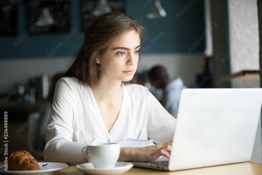 Focused beautiful young girl work at laptop sitting in cafe with coffee and croissant, serious female student using computer studying with books in coffeeshop, millennial woman busy with gadget Focused beautiful young girl work at laptop sitting in cafe with coffee and croissant, serious female student using computer studying with books in coffeeshop, millennial woman busy with gadget