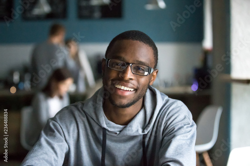 Portrait of smiling African American student looking at camera sitting in cafe, black millennial man posing making picture in coffeeshop, afro male in glasses drinking coffee working in coffeehouse