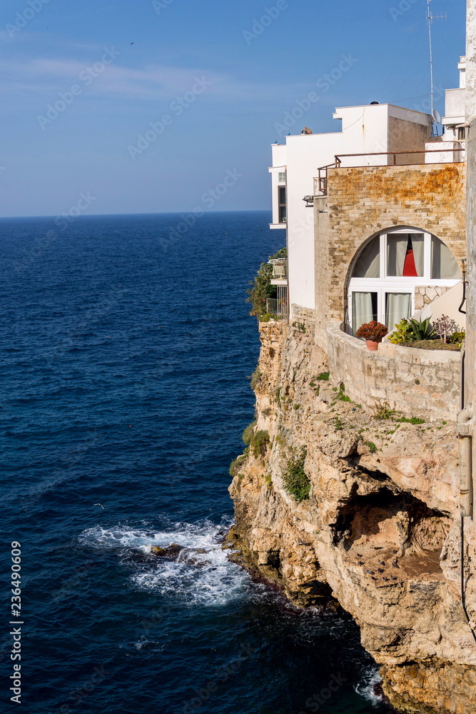 Traditional houses on dramatic cliffs with caves rising from Adriatic sea in Polignano a Mare, Italy, sunny summer day