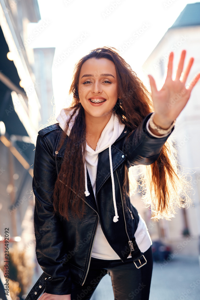 beautiful young woman walking city having fun. joyful Woman in black leather biker jacket and white hoodie laughing and extending hand to the camera Stock Photo Adobe Stock