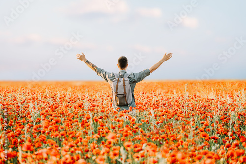 Happy traveler man standing in poppies flowers meadow.