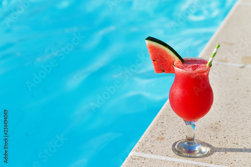 Glass of fresh watermelon smoothie juice drink on border of a swimming pool