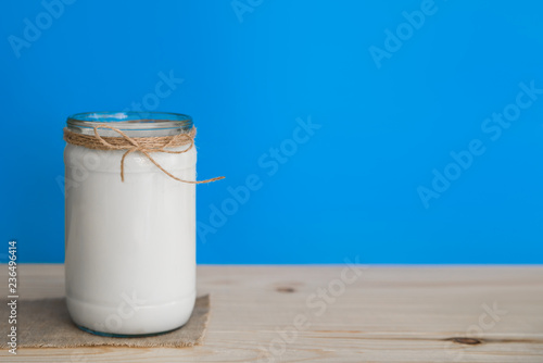 A bottle of rustic milk and glass of milk on a wooden table on a blue background, nutritious and healthy dairy products concept, farm natural products