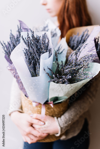 Fototapeta Naklejka Na Ścianę i Meble -  Very nice young redhead woman holding a bucket with aromatic dry lavender on the grey wall background