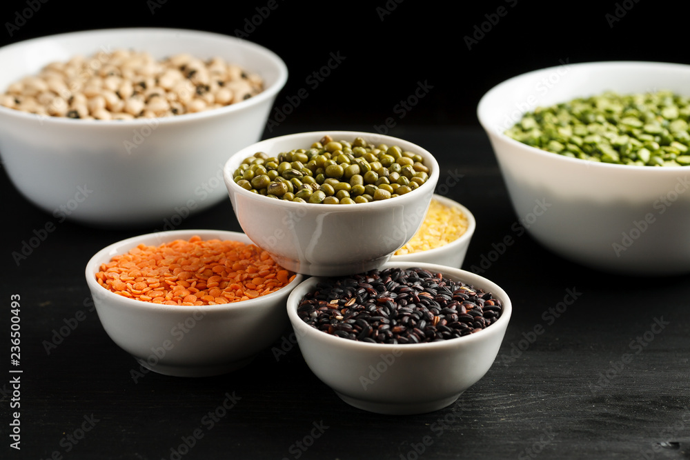 Set of different cereals and legumes in a white bowls on a black table