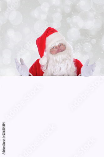 Santa Claus making a gesture with both hands as he stands behind a blank sign