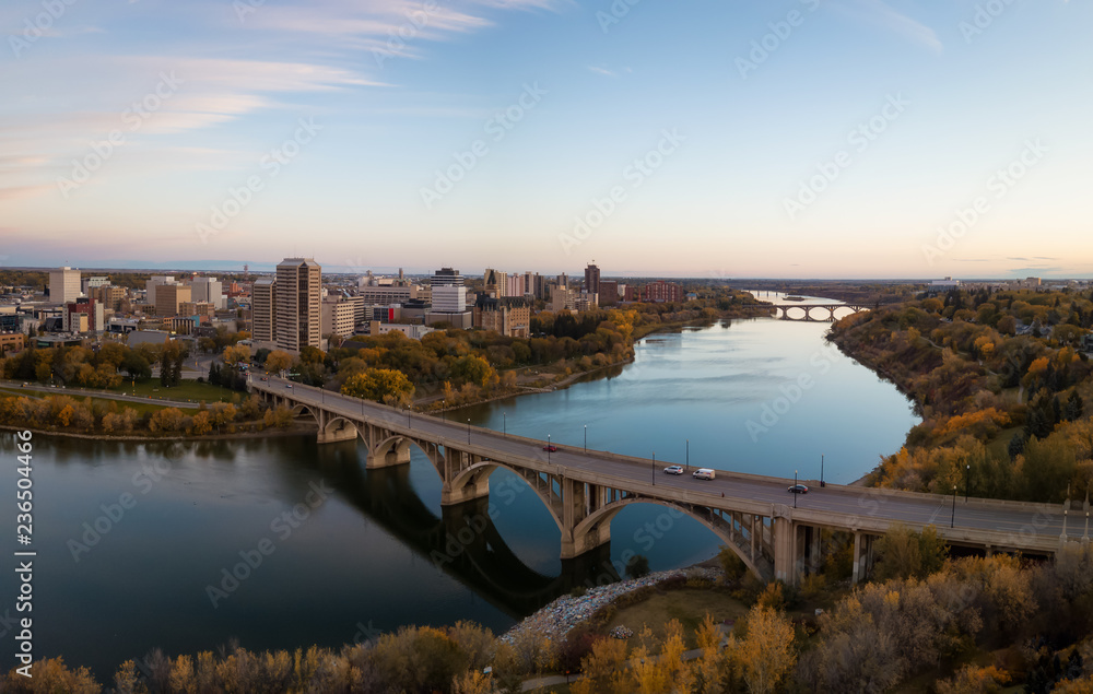 Aerial panoramic view of a bridge going over Saskatchewan River during a vibrant sunrise in the Fall Season. Taken in Saskatoon, SK, Canada.