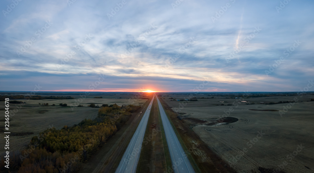Aerial panoramic view of the Highway in the Prairies during a vibrant cloudy sunset. Taken East of Edmonton, Alberta, Canada.