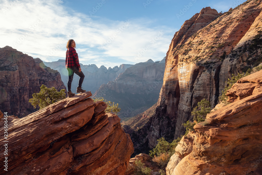 Adventurous Girl at the edge of a cliff is looking at a beautiful landscape view in the Canyon during a vibrant sunset. Taken in Zion National Park, Utah, United States. Adventurous Girl at the edge of a cliff is looking at a beautiful landscape view in the Canyon during a vibrant sunset. Taken in Zion National Park, Utah, United States.