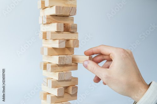 Fényképezés Man's hand taking or putting a block to an unstable and incomplete tower of wooden blocks