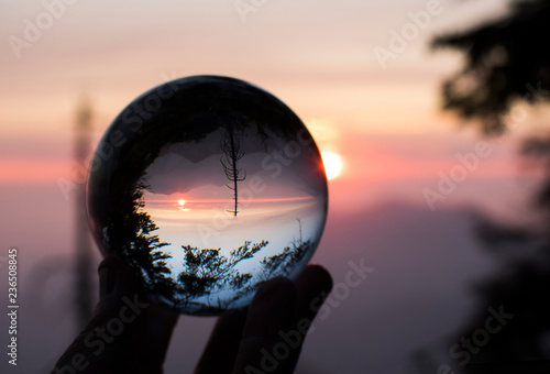 Sunset over Mountain Range with Trees in Silhouette Captured in Glass Globe in Fingertips
