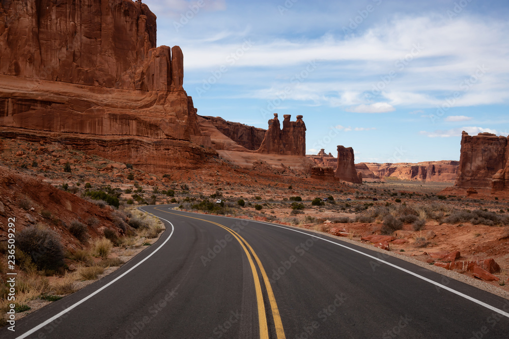 Landscape view of a Scenic road in the red rock canyons during a vibrant sunny day. Taken in Arches National Park, located near Moab, Utah, United States. Landscape view of a Scenic road in the red rock canyons during a vibrant sunny day. Taken in Arches National Park, located near Moab, Utah, United States.