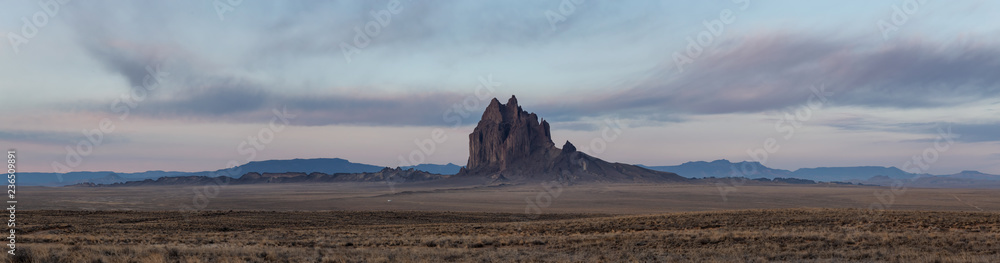 Fotobehang Chocoladebruin Dramatische panoramische landschapsmening van een droge woestijn met een bergtop op de achtergrond tijdens een levendige bewolkte zonsopgang. Genomen op Shiprock, New Mexico, Verenigde Staten. #236509891