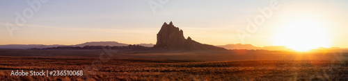 Striking panoramic landscape view of a dry desert with a mountain peak in the background during a vibrant sunset. Taken at Shiprock, New Mexico, United States. © edb3_16