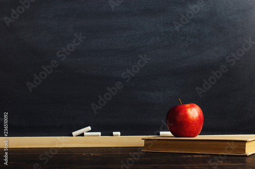 Black chalk board over wooden table with a book and an apple, blank for text or background for a school theme.