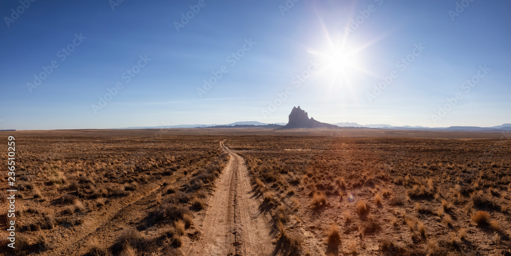 Striking panoramic landscape view of a dirt road in the dry desert with a mountain peak in the background. Taken at Shiprock, New Mexico, United States.