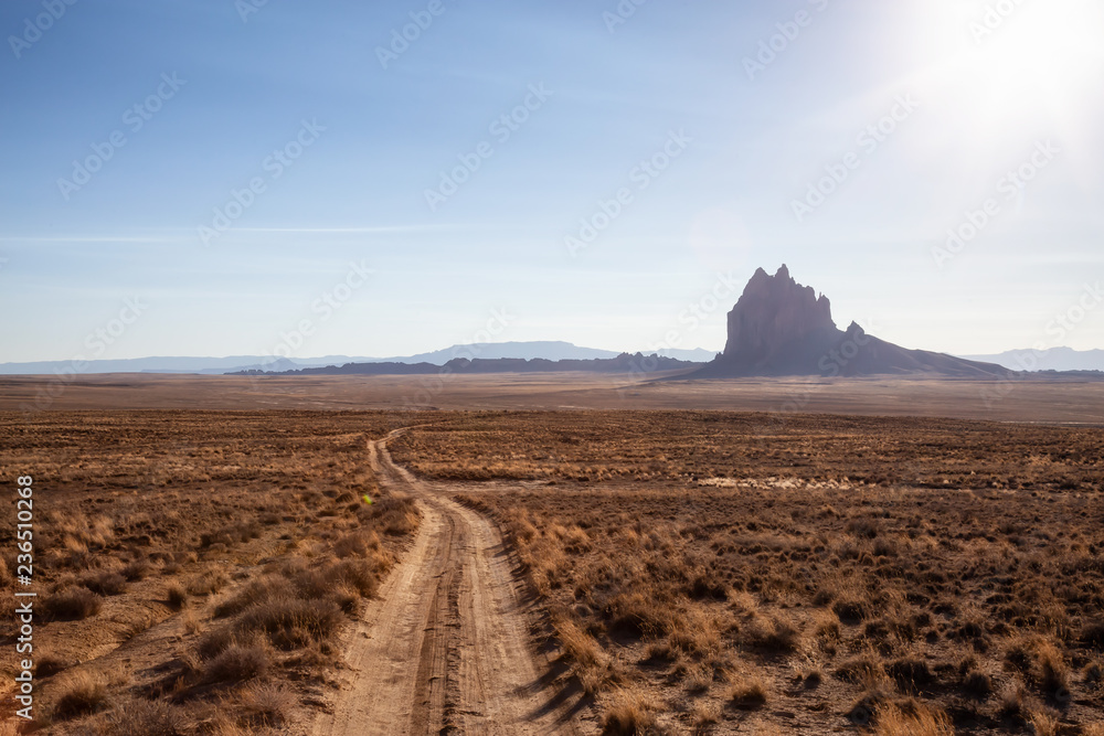 Striking landscape view of a dirt road in the dry desert with a mountain peak in the background. Taken at Shiprock, New Mexico, United States. Striking landscape view of a dirt road in the dry desert with a mountain peak in the background. Taken at Shiprock, New Mexico, United States.
