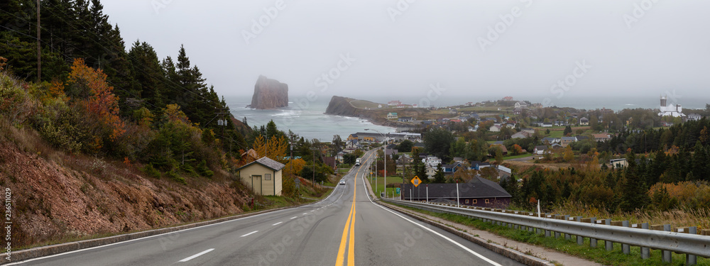 Panoramic view of a road leading to a beautiful modern town on the Atlantic Ocean Coast during a hazy day. Taken in Percé, Quebec, Canada.