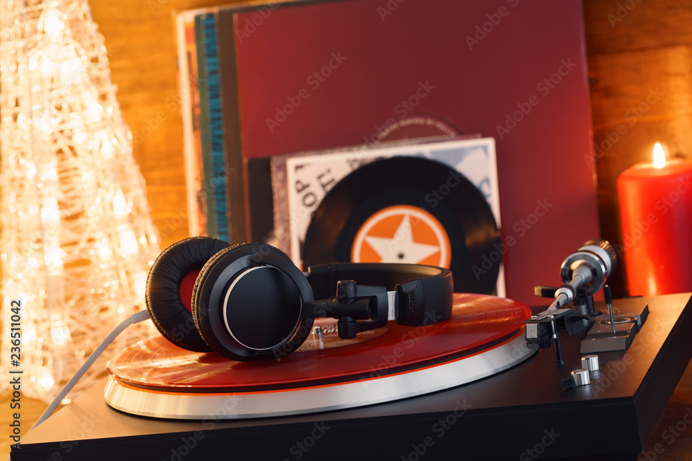Fototapeta premium Turntable player with black headphones on the background of a stack of audition records and a Christmas tree. Sound technology for DJ to mix and play music. Red vinyl record and stylus with needle