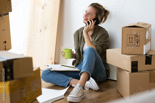 Pretty young woman talking on her mobile phone while sitting on her new house. photo