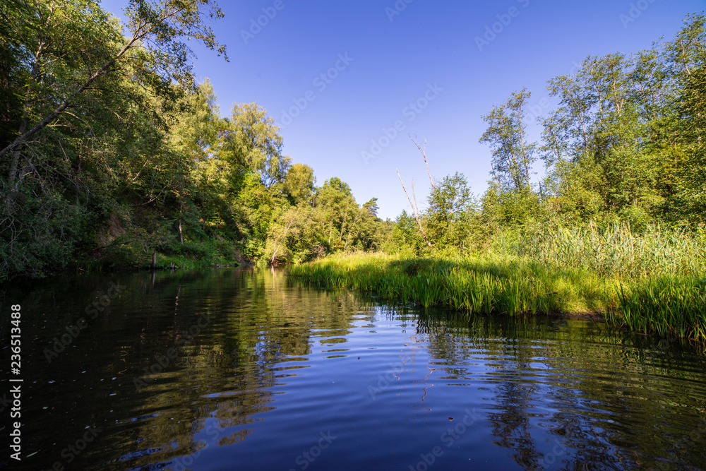 summer day on water in calm river enclosed in forests with sandstone cliffs and dry wood