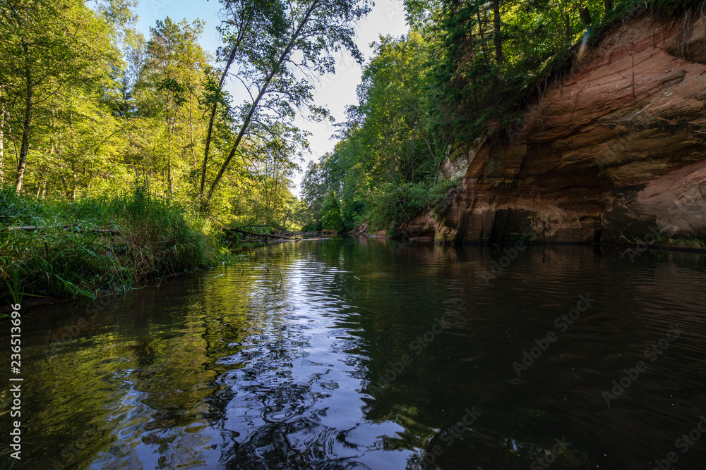 summer day on water in calm river enclosed in forests with sandstone cliffs and dry wood