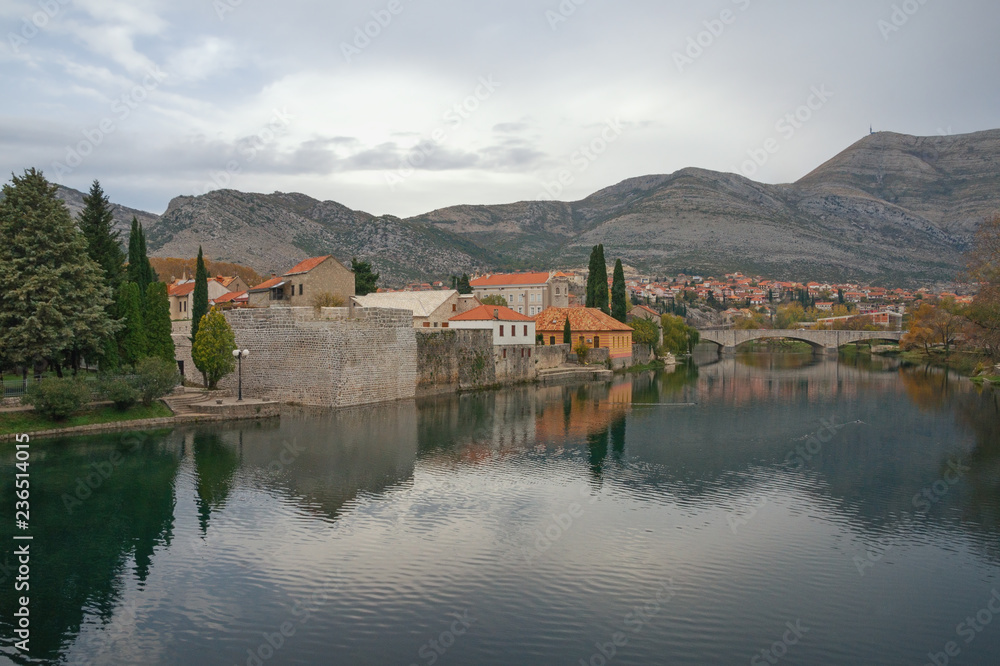 Cloudy autumn landscape. Town on river bank reflected in water. Bosnia and Herzegovina. View of Trebisnjica river and Trebinje city Cloudy autumn landscape. Town on river bank reflected in water. Bosnia and Herzegovina. View of Trebisnjica river and Trebinje city