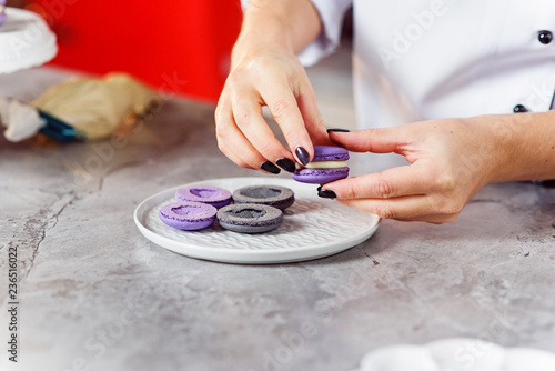 The confectioner joins the parts of the macarons with each other using a cream. Close up baker hands making macarons.